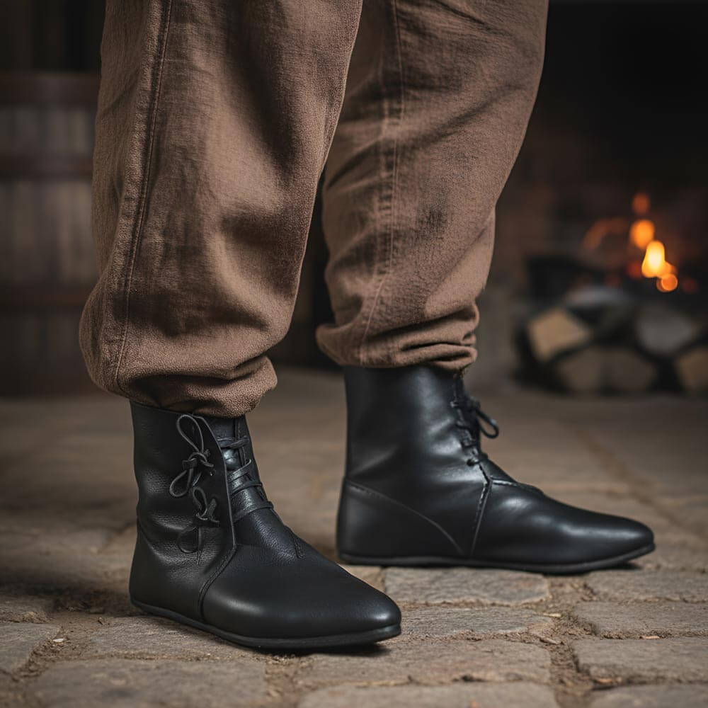Person wearing Black Leather Viking Ankle Boots with Four-String Adjustment and brown pants standing in front of a fireplace.