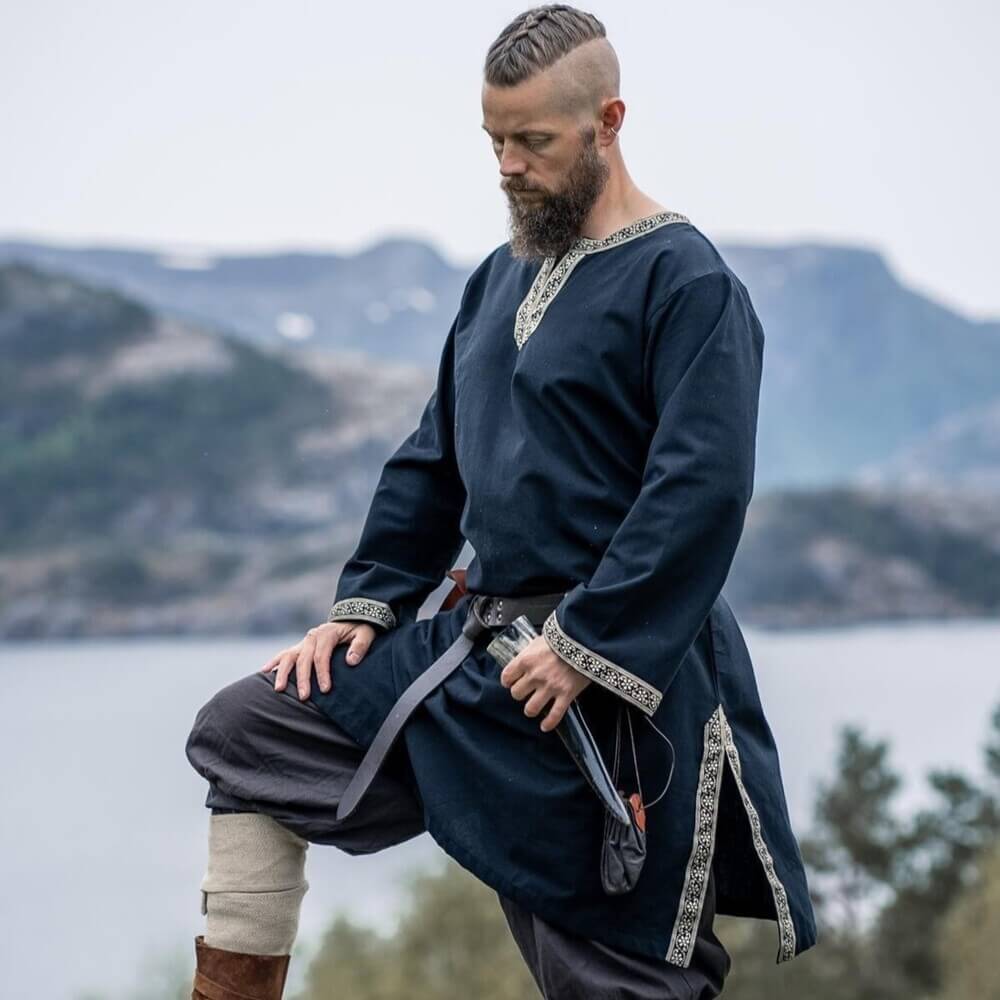 Black Viking tunic with embroidered border, knee-length, worn by a man outdoors.