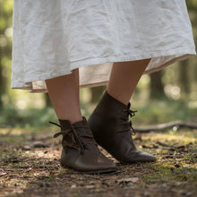 Brown leather boots worn with a white skirt in a forest setting