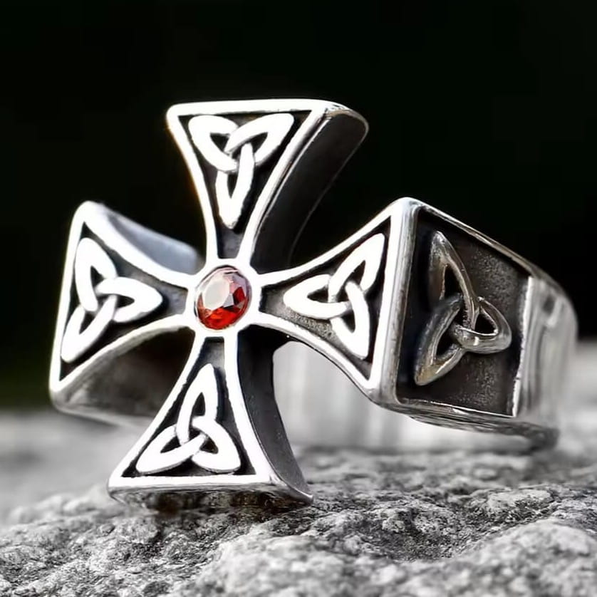 Celtic Trinity knot cross ring with red garnet stone in antiqued stainless steel displayed on gray stone