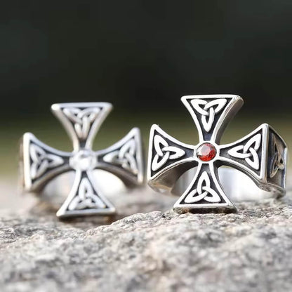 Viking Celtic Trinity Cross rings, silver-tone, one with red stone, one with clear stone, on rock.