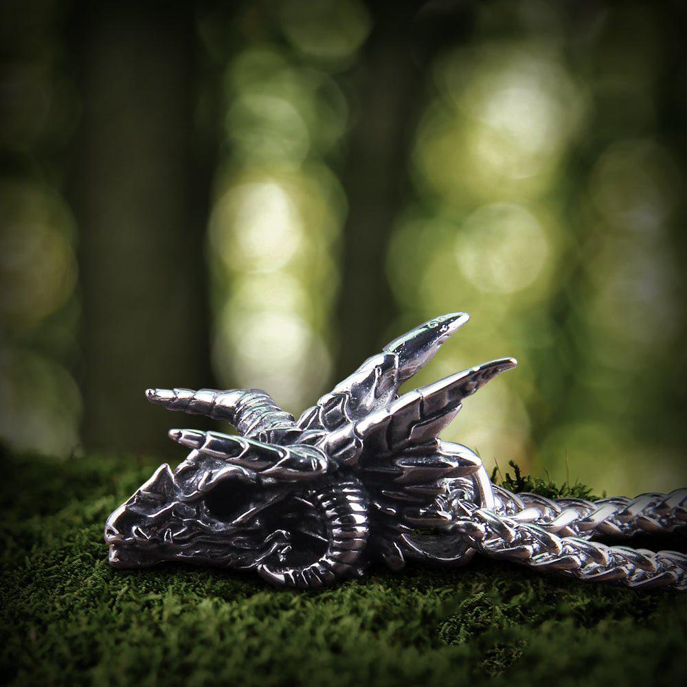 Viking dragon skull steel pendant, detailed silver-tone, resting on green moss.