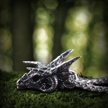 Viking dragon skull steel pendant, detailed silver-tone, resting on green moss.