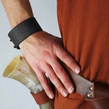 Black embossed Viking leather bracelet on a man's wrist, with a drinking horn and brown leather strap.