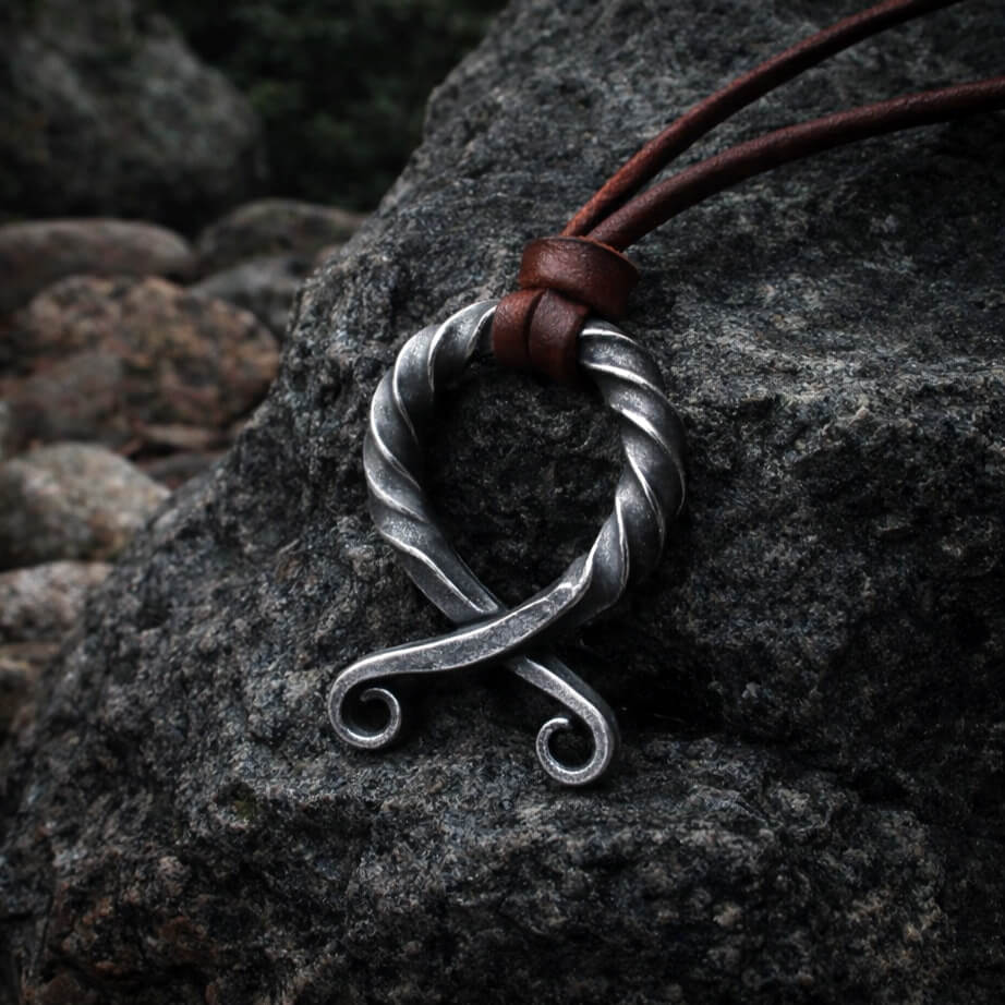 Viking forged iron antiqued Troll Cross pendant with brown leather cord on a dark rock.