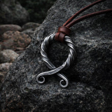 Viking forged iron antiqued Troll Cross pendant with brown leather cord on a dark rock.