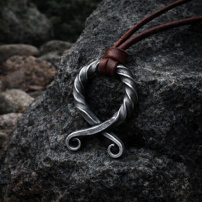 Viking forged iron antiqued Troll Cross pendant with brown leather cord on a dark rock.