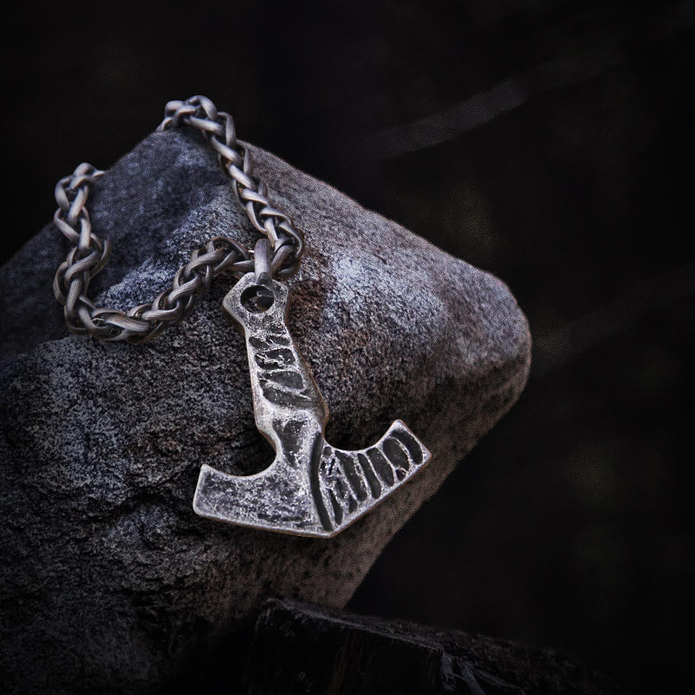 Blackened steel Viking Thor's Hammer necklace with a braided chain, resting on a dark stone.