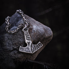 Blackened steel Viking Thor's Hammer necklace with a braided chain, resting on a dark stone.