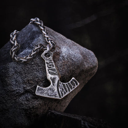 Blackened steel Viking Thor's Hammer necklace with a braided chain, resting on a dark stone.