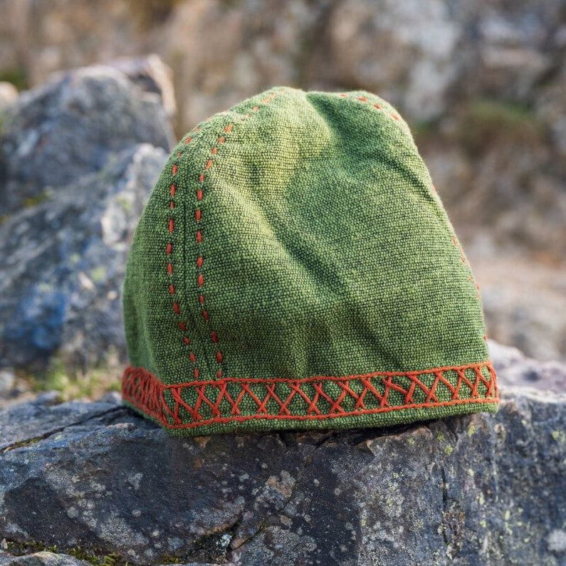 Green cotton Viking cap with red embroidered Norse motifs on a rock.