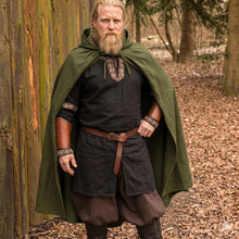 Viking warrior in a hooded, dark green wool cloak over a black tunic with embroidered trim and brown leather bracers.