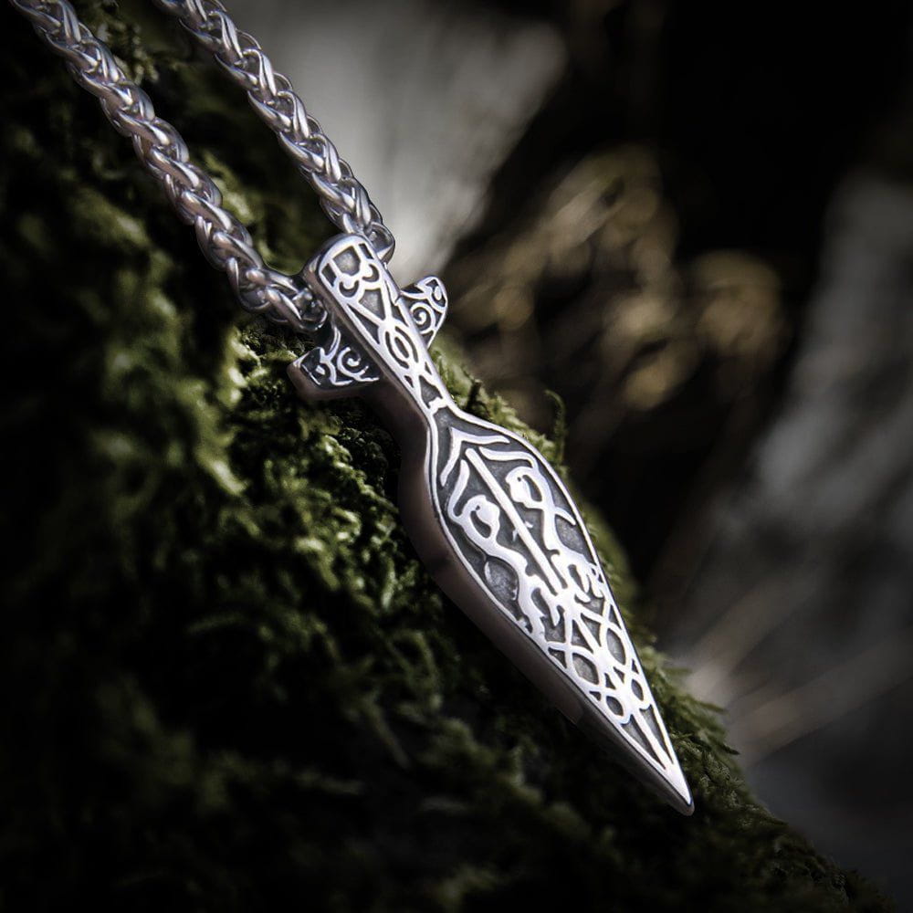 Silver Viking spearhead necklace with intricate knotwork design on a mossy surface.