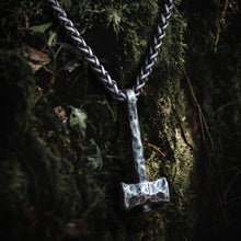 Viking hammered iron Thor's Hammer Mjolnir pendant on a thick chain, against mossy bark.
