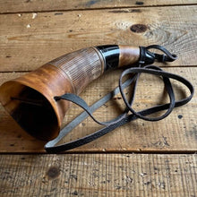 Handcrafted Viking blowing horn, natural brown with black mouthpiece and leather strap on wood.