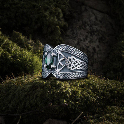Sterling silver Viking ring with a green emerald and intricate Celtic knotwork on moss.