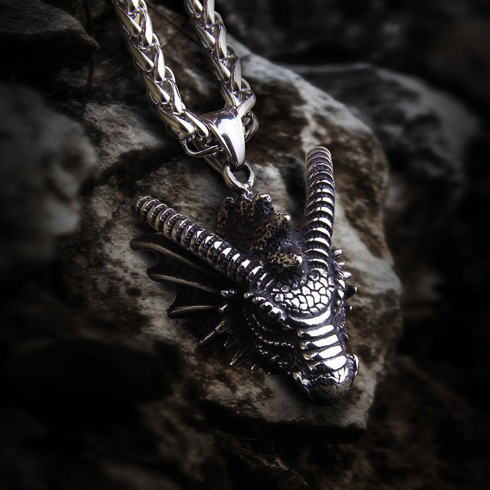 Heavy steel Viking dragon bust pendant on a thick silver chain, resting on a rock.