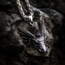 Heavy steel Viking dragon bust pendant on a thick silver chain, resting on a rock.