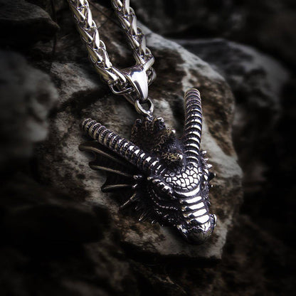 Heavy steel Viking dragon bust pendant on a thick silver chain, resting on a rock.