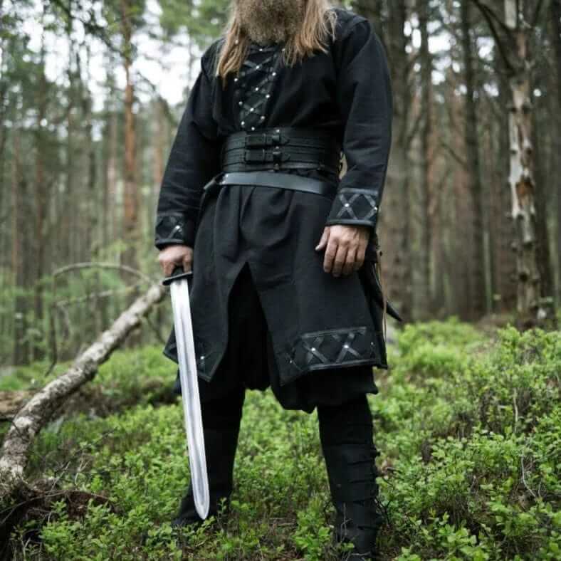 Black Viking tunic with leather trim, rivets, and decorative stitching, worn by a bearded man holding a sword.