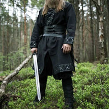 Black Viking tunic with leather trim, rivets, and decorative stitching, worn by a bearded man holding a sword.