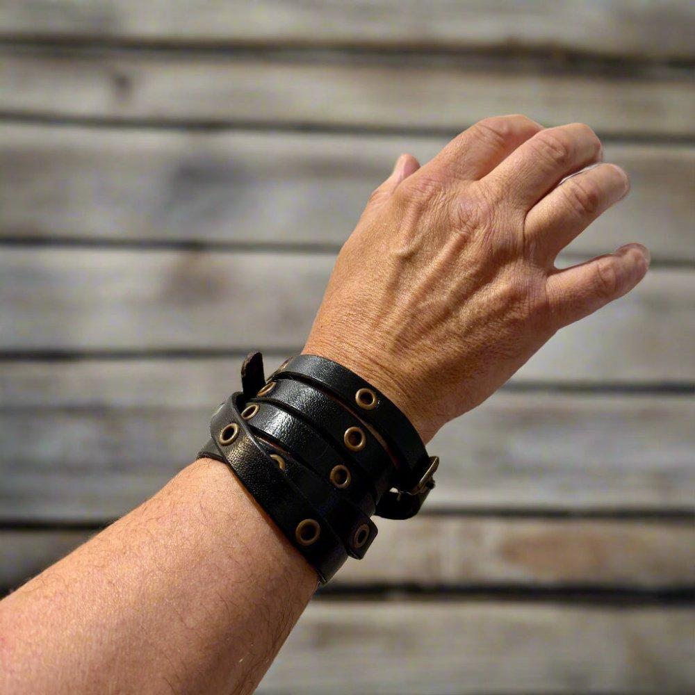 Black leather multi-wrap Viking bracelet with brass rivets and buckle closure on a wrist.