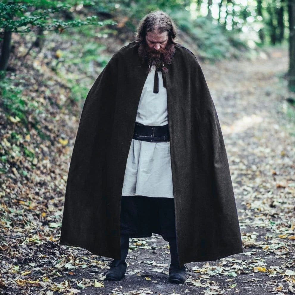 Man in a long, dark Viking hooded wool cloak with adjustable closure, standing in a forest.