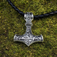Silver Viking Mjolnir pendant with intricate knotwork on a black braided rope necklace, resting on moss.