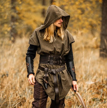 Viking-style hooded green tunic with leather belt, bracers, and bow in a forest.
