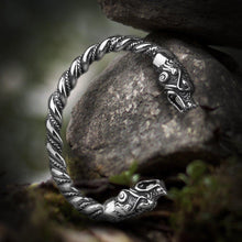 Silver Viking twisted steel torc bracelet with detailed bear heads, resting on rocks.
