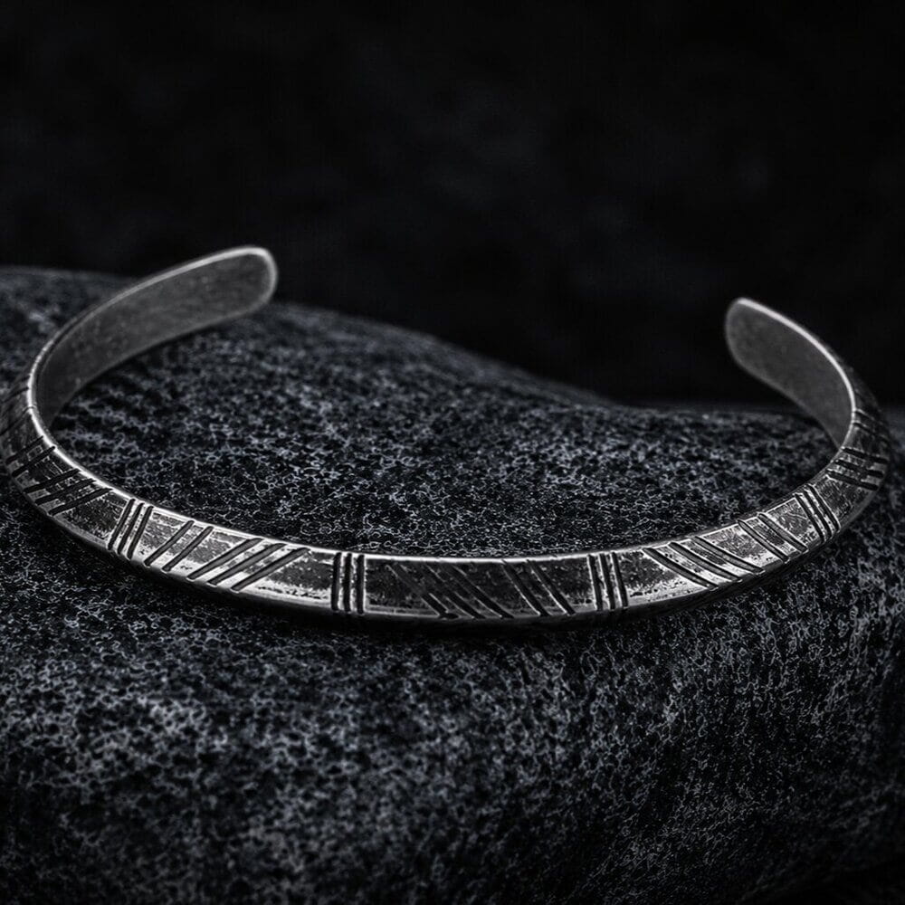 Viking Nordic Tyr Arrow silver-tone cuff bracelet with engraved open band on a dark textured surface.