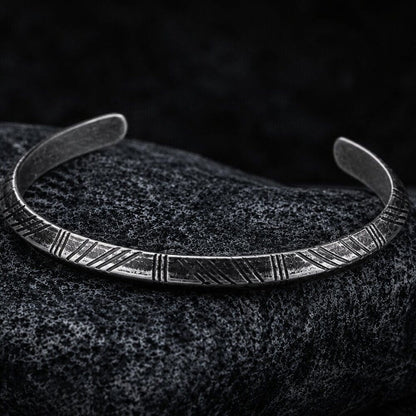 Viking Nordic Tyr Arrow silver-tone cuff bracelet with engraved open band on a dark textured surface.