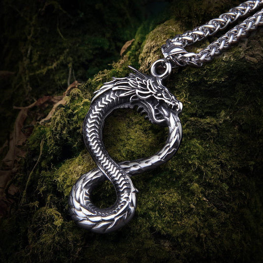 Viking Norse Jörmungandr dragon necklace in silver-tone steel, coiled in an infinity shape on moss.