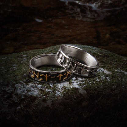 Two bold steel Viking Futhark rune rings on a mossy rock; one with gold runes, one with silver.