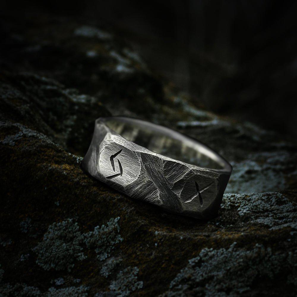Rough hewn silver Viking warrior ring with etched runes on a dark, textured surface.