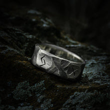 Rough hewn silver Viking warrior ring with etched runes on a dark, textured surface.