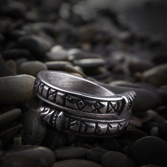 Silver Viking ring with Futhark runes and Midgard Serpent design on dark pebbles.