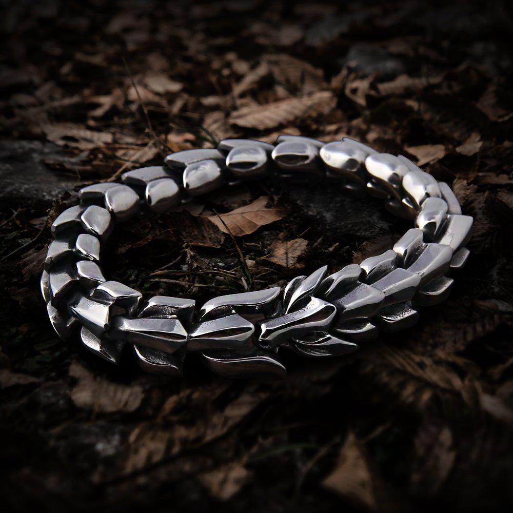 Silver Viking Jormungandr dragon bracelet with scale links on a bed of fallen leaves.