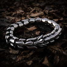 Silver Viking Jormungandr dragon bracelet with scale links on a bed of fallen leaves.