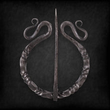 Dark twisted steel Viking penannular cloak clasp with decorative scrolls and a sharp pin.