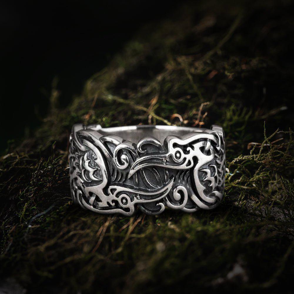 Handcrafted sterling silver Viking ring with intricate raven and ornate scrollwork on moss.