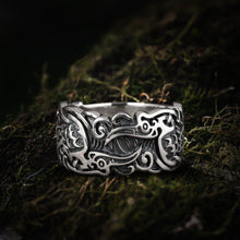 Handcrafted sterling silver Viking ring with intricate raven and ornate scrollwork on moss.