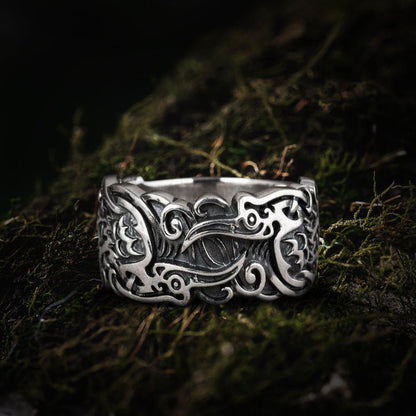 Handcrafted sterling silver Viking ring with intricate raven and ornate scrollwork on moss.