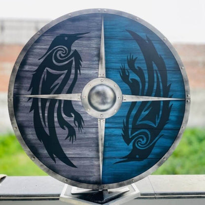 Round Viking shield with split blue and grey wood grain, featuring two black raven designs and a central metal boss.