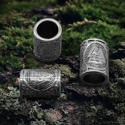 Set of 3 silver Viking Valknut beard beads with intricate knotwork on mossy wood.