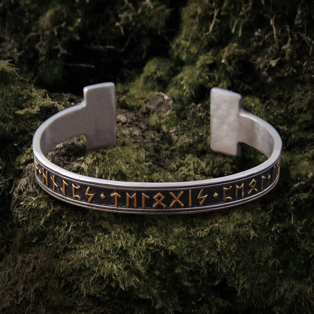Silver steel Viking Futhark rune bangle bracelet with gold stamped symbols on a dark moss background.