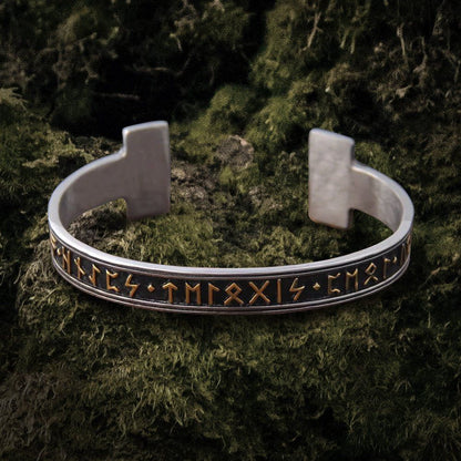 Silver steel Viking Futhark rune bangle bracelet with gold stamped symbols on a dark moss background.