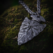 Dark gray Viking Helm of Awe arrowhead pendant on a braided chain, resting on green moss.