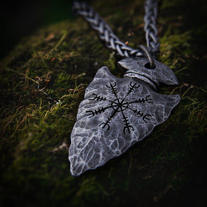 Dark gray Viking Helm of Awe arrowhead pendant on a braided chain, resting on green moss.