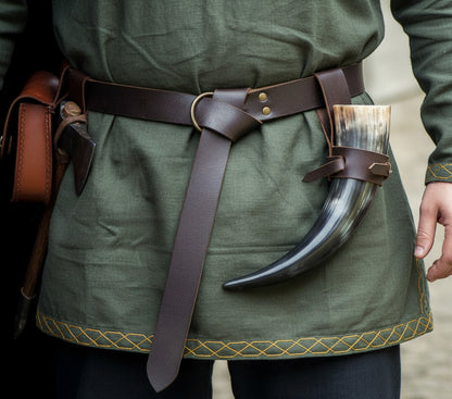 Person wearing a thick brown leather Viking belt with ring loop and knot on a green tunic with horned accessory.